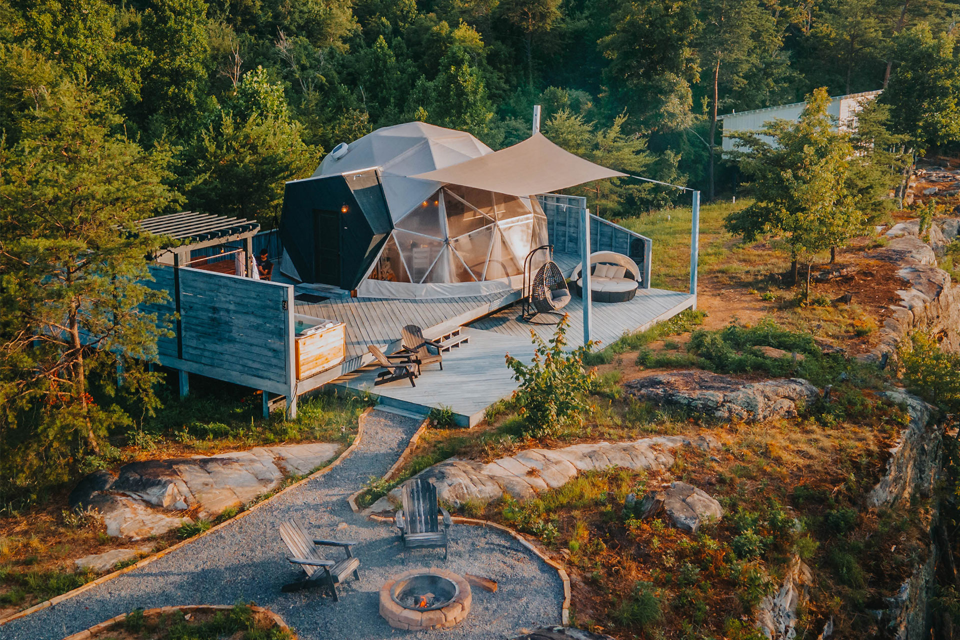 Exterior of a dome with curved glass tucked into the woods at BOLT FARM, a private fire pit nearby